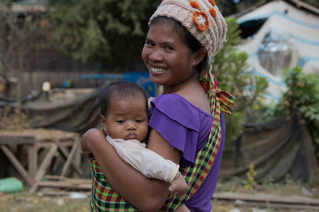 A woman wearing a purple shirt smiles and holds her baby.
