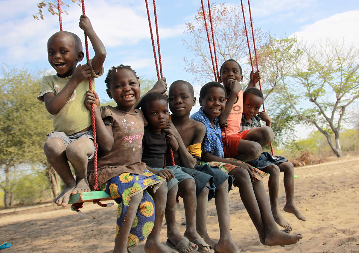 A group of kids smile and laugh while sitting on a large green swing.