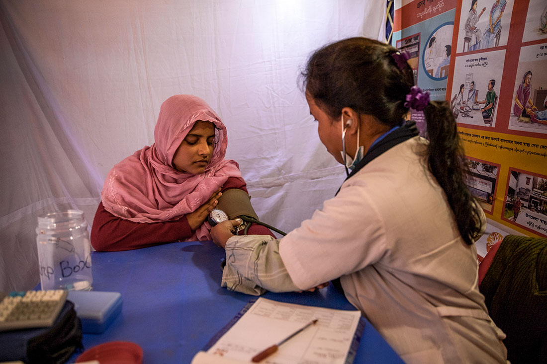 A female doctor takes the blood pressure of a woman sitting across the table from her.