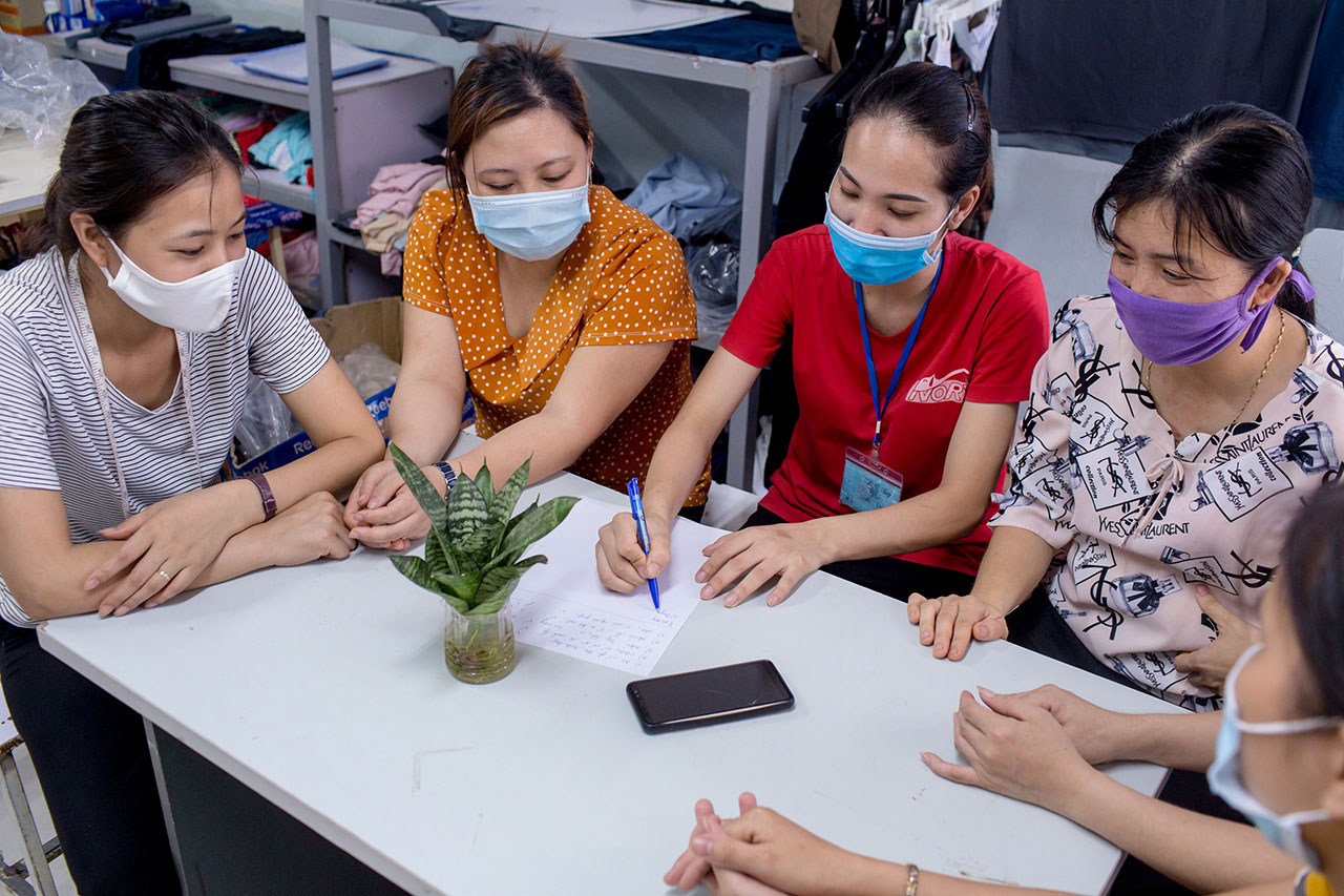 A group of women, all wearing face masks, sit together around a table.